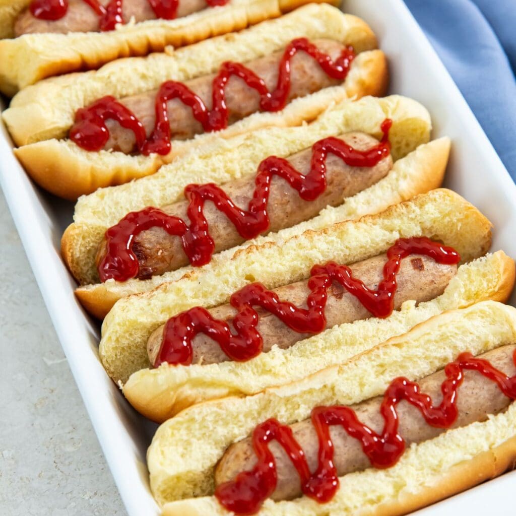 chicken sausage in buns with ketchup on it. blue towel next to it