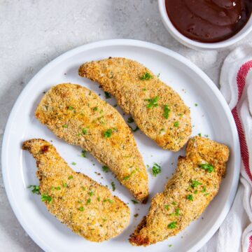 white plate with chicken on it. parsley and white a, pink towel in the back bbq sauce next to it