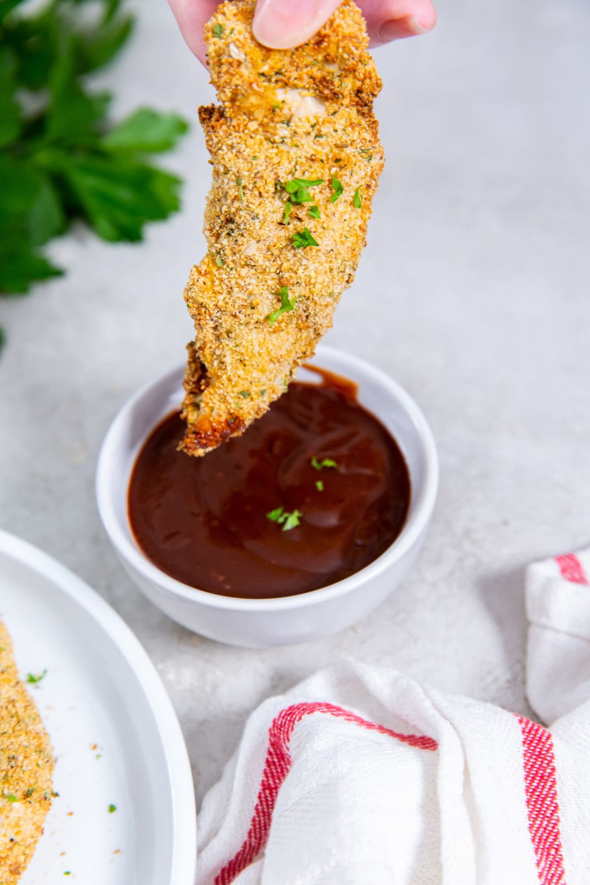 chicken being held over bbq sauce. parsley inn the back