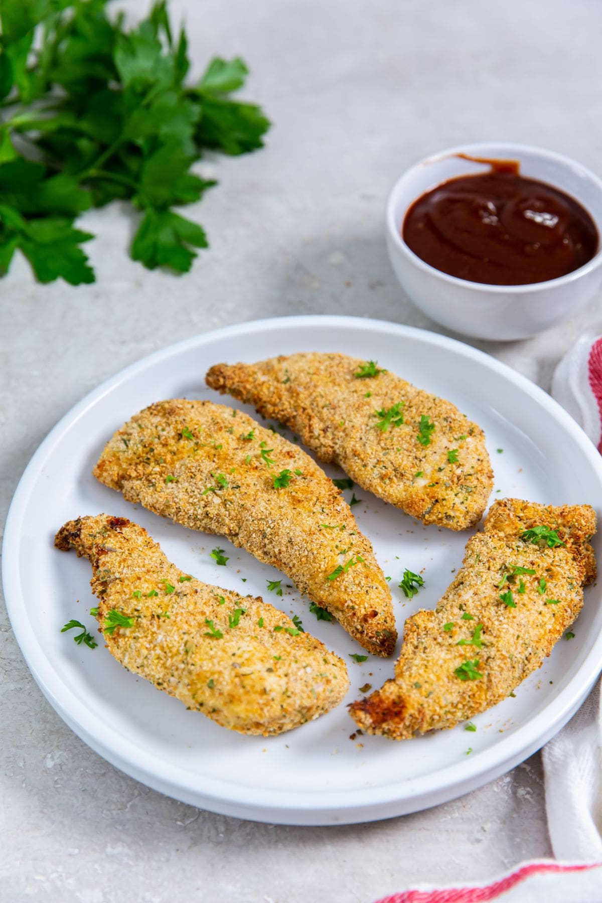 white plate with chicken on it. parsley and white , pink towel and bbq in the back