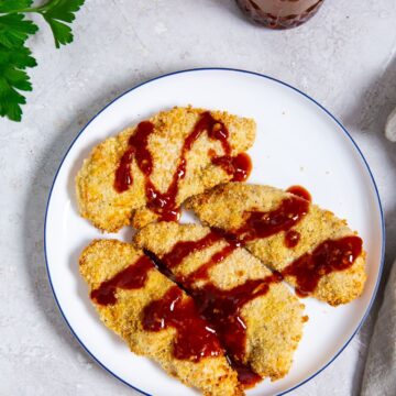 white plate with katsu sauce onto of the chicken. parsley and mason jar in the back