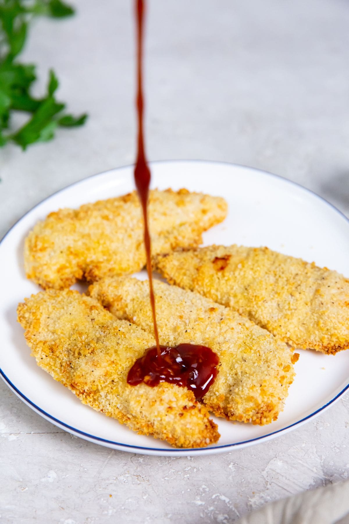 white plate with katsu sauce being poured on the chicken