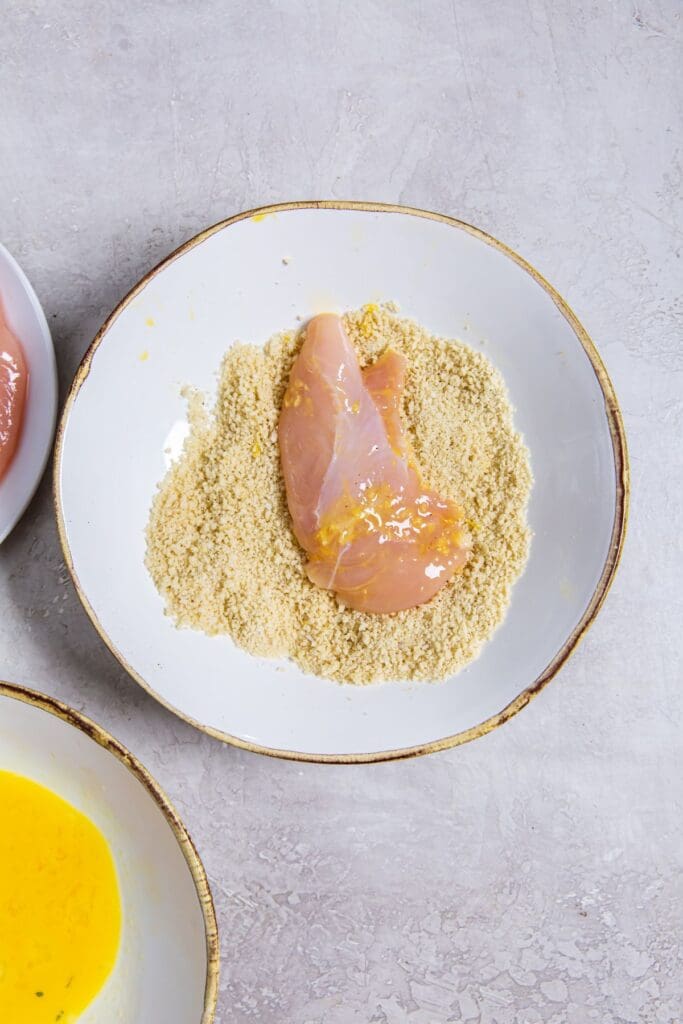 chicken tenders in white bowl dunked in breadcrumbs