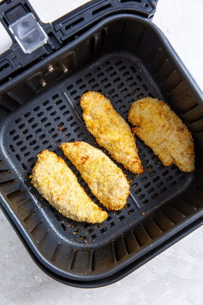 black air fryer basket with cooked chicken Inside