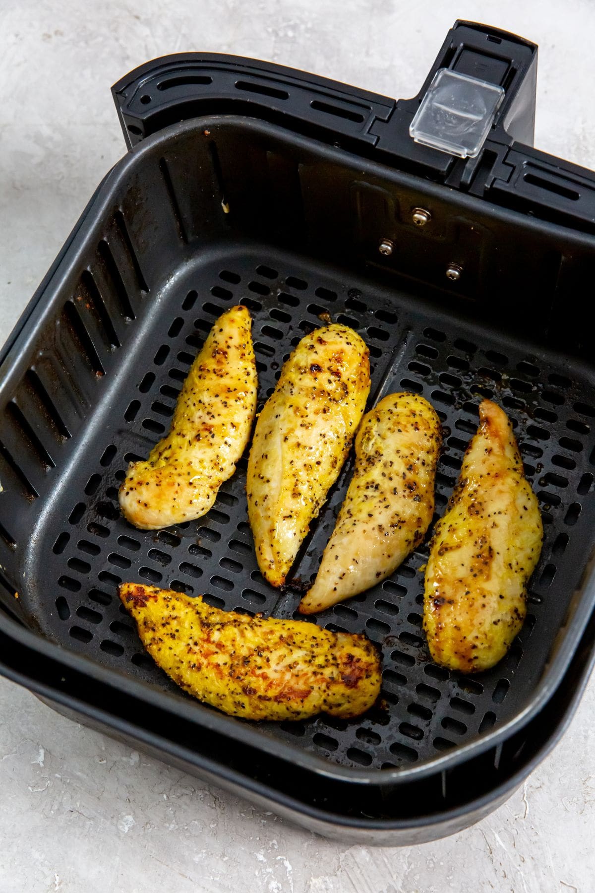 black air fryer basket with cooked chicken inside