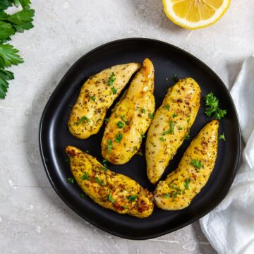 black plate with chicken on it. parsley, lemon, white towel in the back.