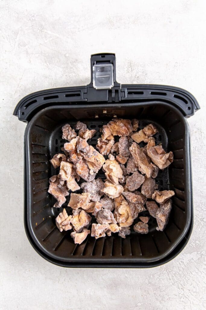 black air fryer with frozen chicken inside