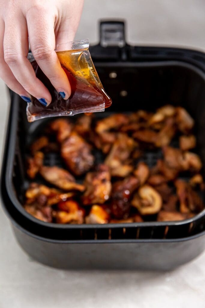 black air fryer basket with cooked chicken inside. sauce being poured over the top