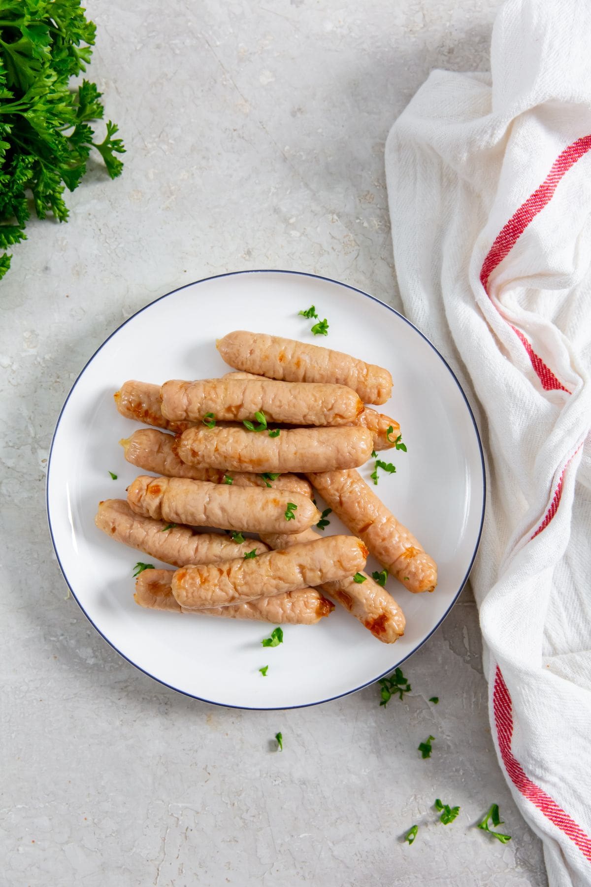 white plate with chicken sausages on them. parsley and white towel in the back