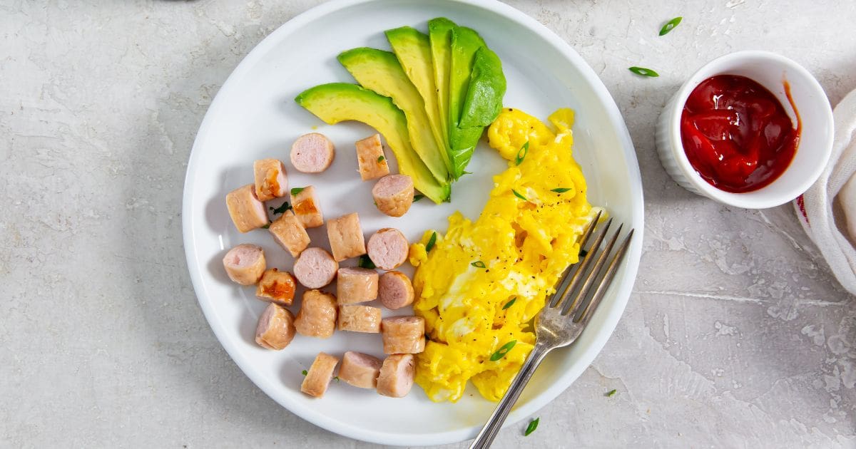 plate with sausage, eggs, and avocado slices.