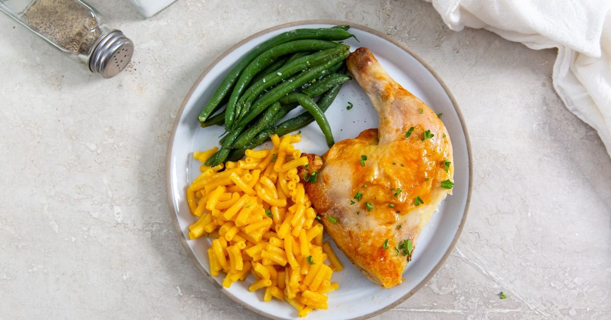 White plate with chicken Mac and cheese, and green beans on it. white towel in the back