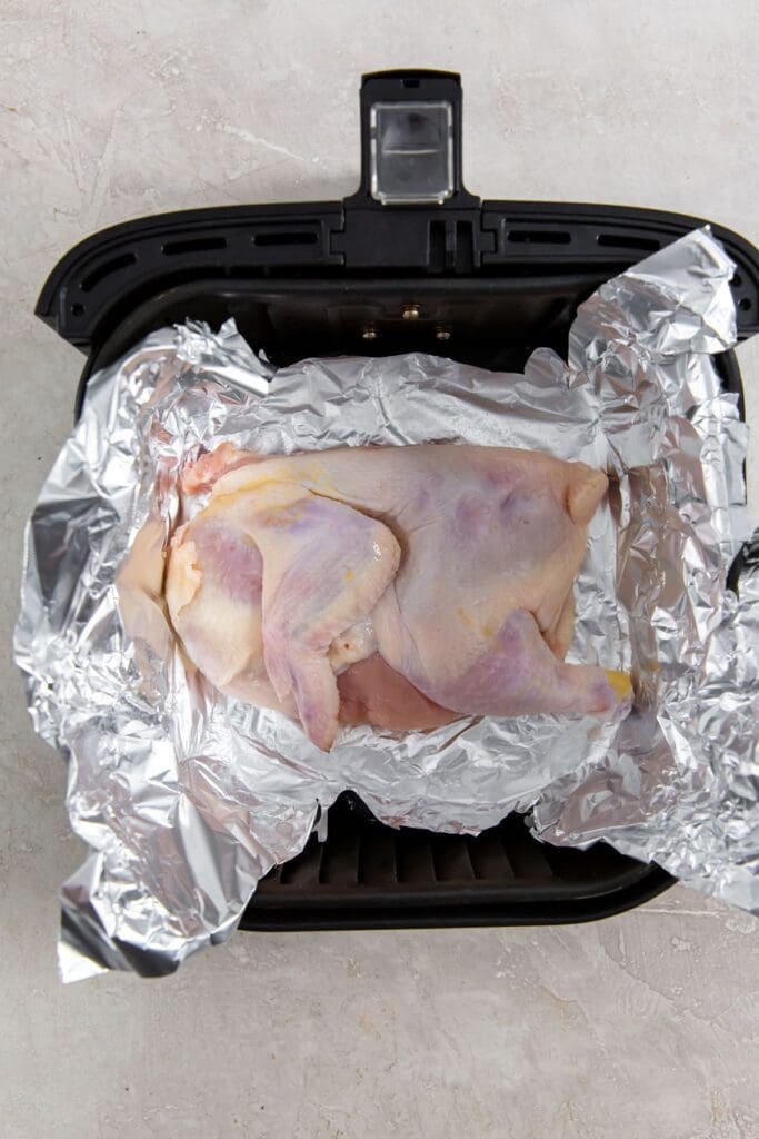 black air fryer basket with aluminum foil. half chicken inside.