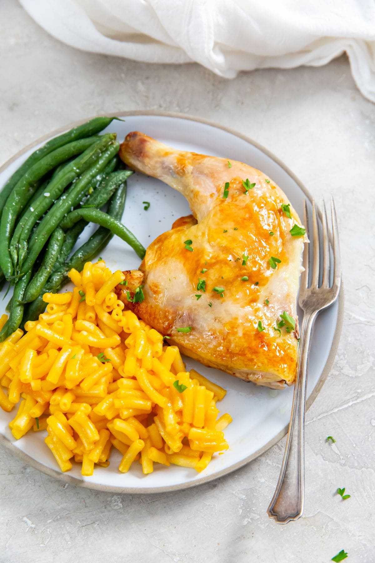 White plate with chicken Mac and cheese, and green beans on it. fork on the side. white towel in the back