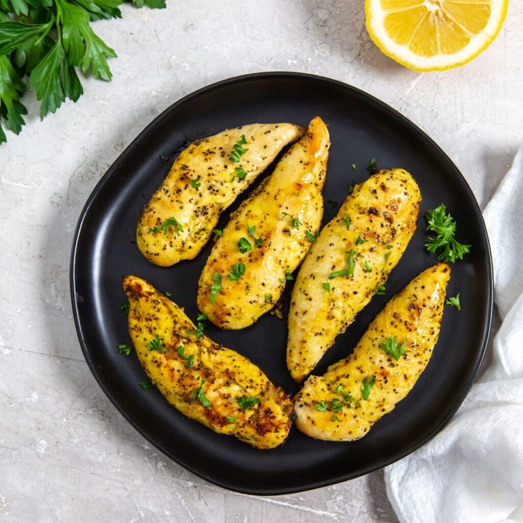 black plate with chicken on it. parsley, lemon, white towel in the back.