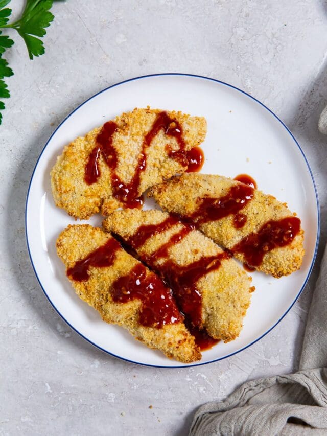 white plate with katsu sauce onto of the chicken. parsley and mason jar in the back