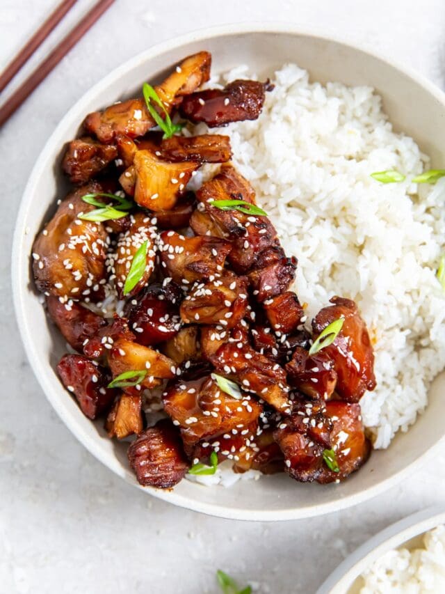 two bowls with chicken and rice inside them. gray towel in the back along with chopsticks and sesame seeds