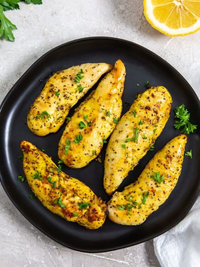 black plate with chicken on it. parsley, lemon, white towel in the back.