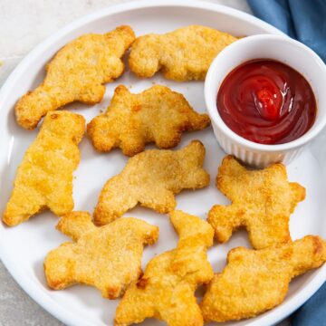 white plate with chicken fries and ketchup. parsley and gray towel in the back