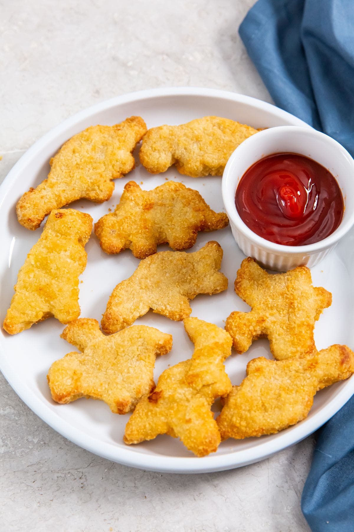 white plate with chicken fries and ketchup. parsley and gray towel in the back