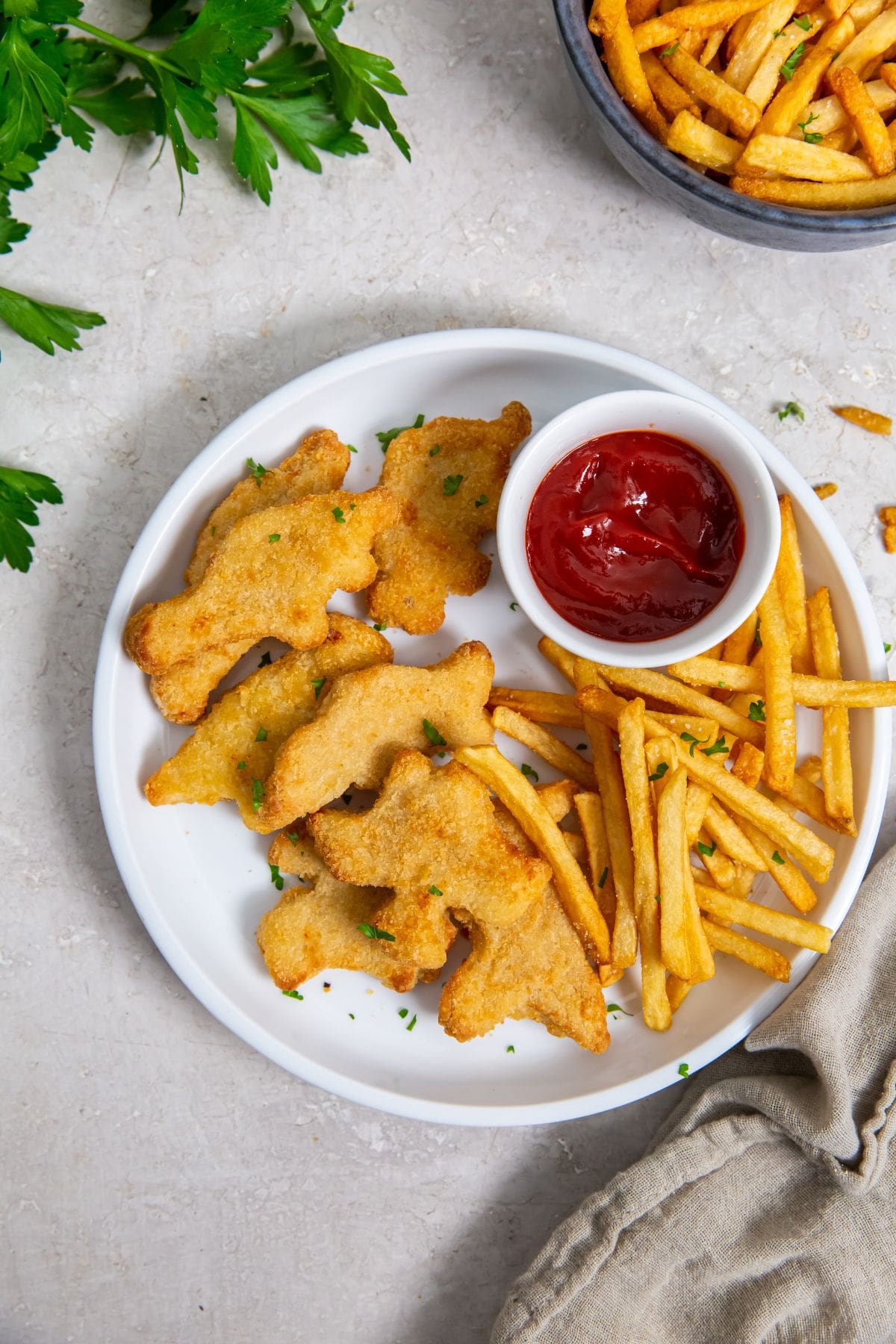 white plate with chicken fries and ketchup. parsley and gray towel in the back