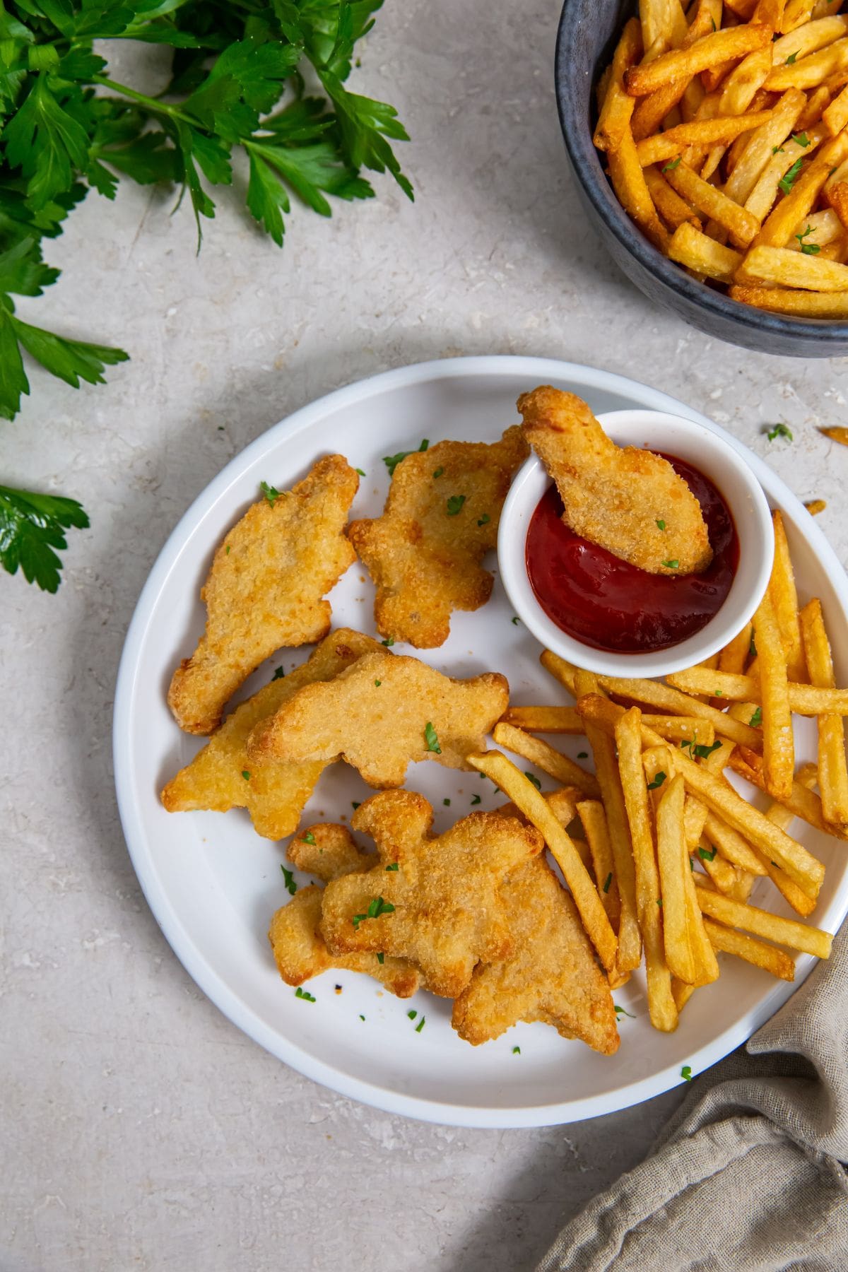 white plate with chicken fries and ketchup. parsley and gray towel in the back