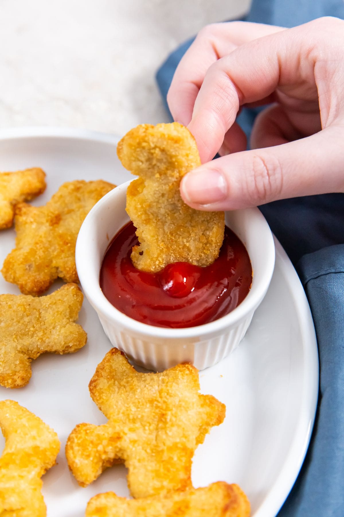 white plate with chicken fries and ketchup. parsley and gray towel in the back