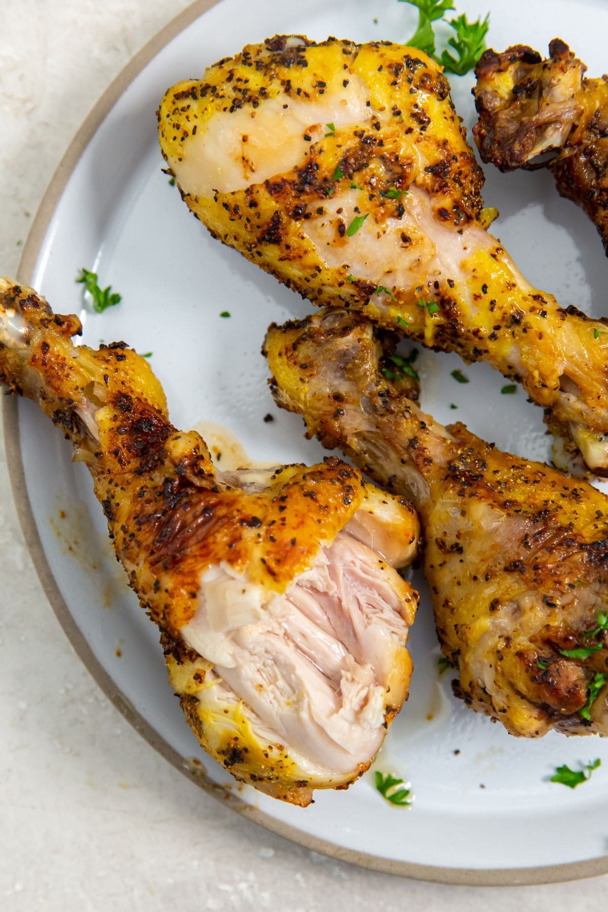 white plate with chicken legs on them. parsley sprinkled on top. Parsley in the back