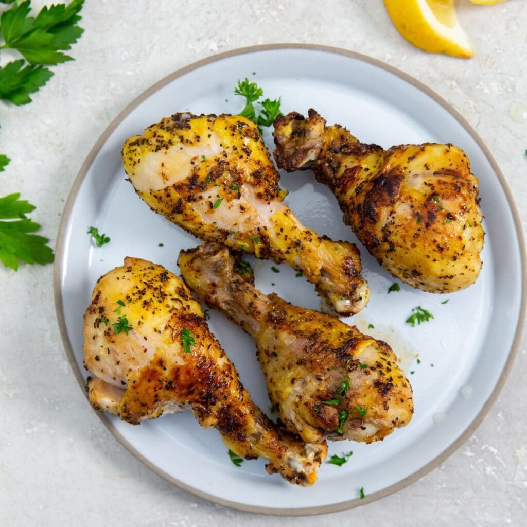 white plate with chicken legs on them. parsley sprinkled on top. Parsley in the back