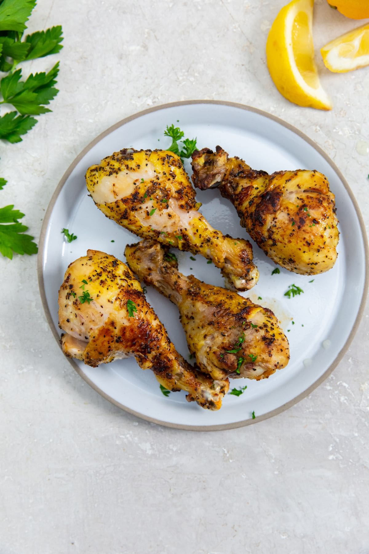 white plate with chicken legs on them. parsley sprinkled on top. Parsley in the back