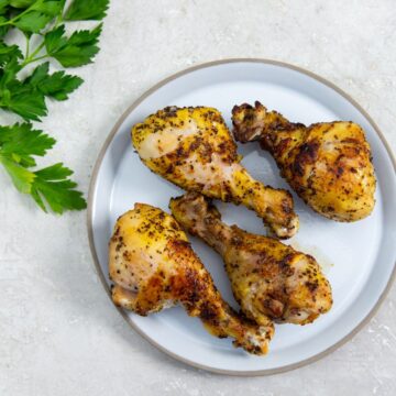 white plate with chicken legs on them. parsley sprinkled on top. Parsley in the back