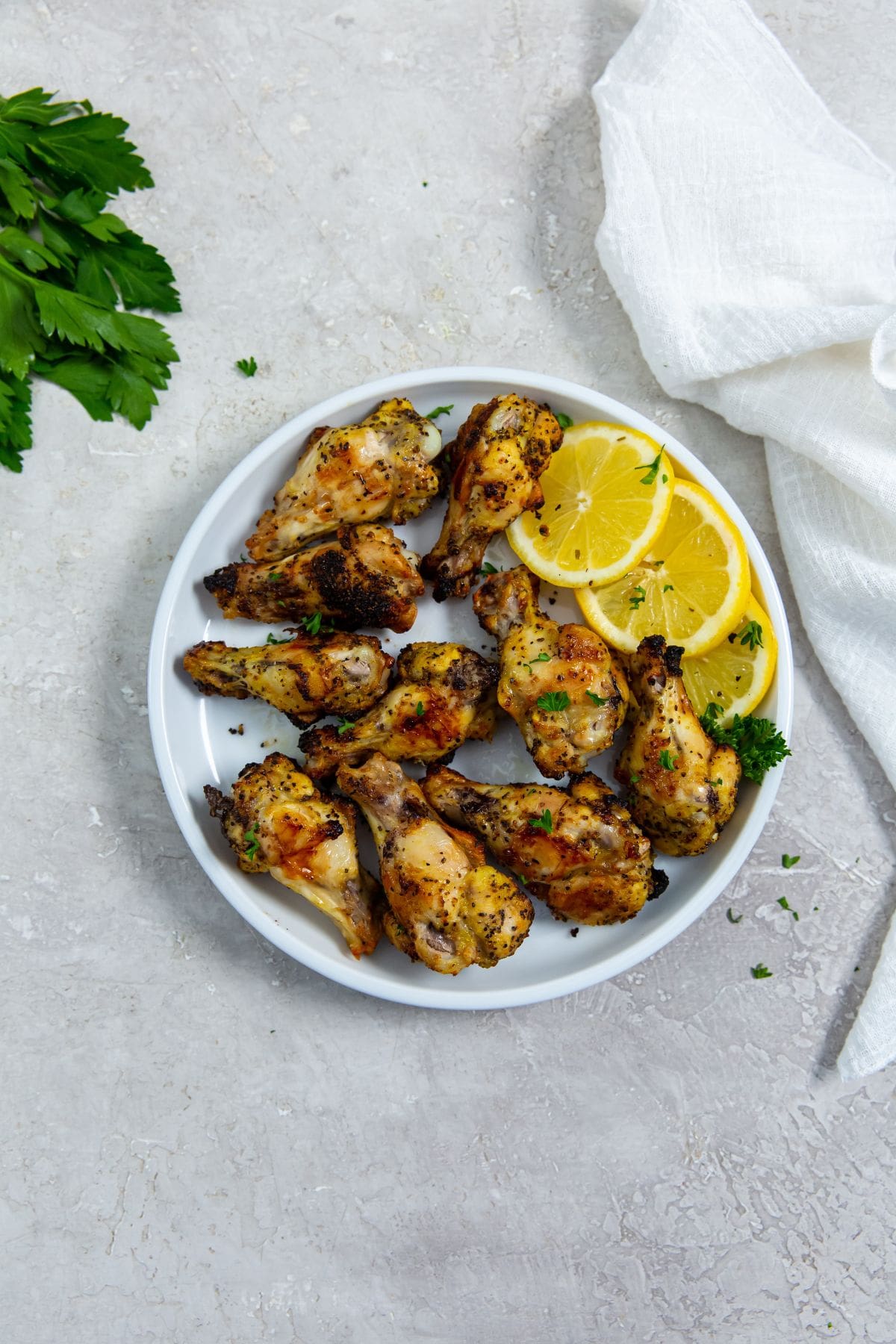 white plate with chicken and lemons on it. parsley in the back.