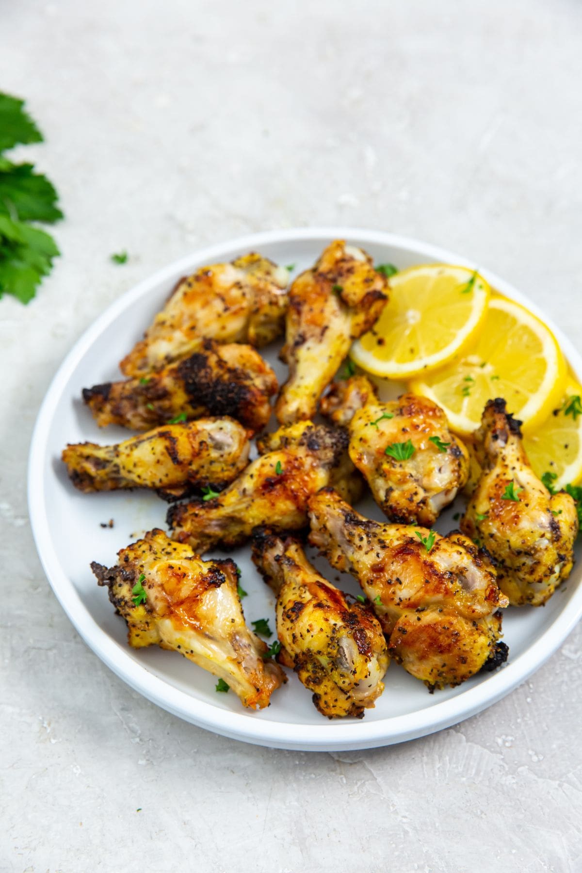 white plate with chicken and lemons on it. parsley in the back.