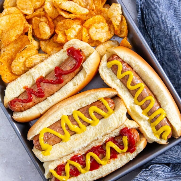 tray with chicken in a hotdog bun mustard and ketchup on top. chips on the side. blue towel behind it.