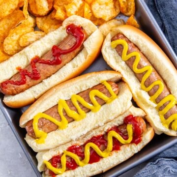 tray with chicken in a hotdog bun mustard and ketchup on top. chips on the side. blue towel behind it.