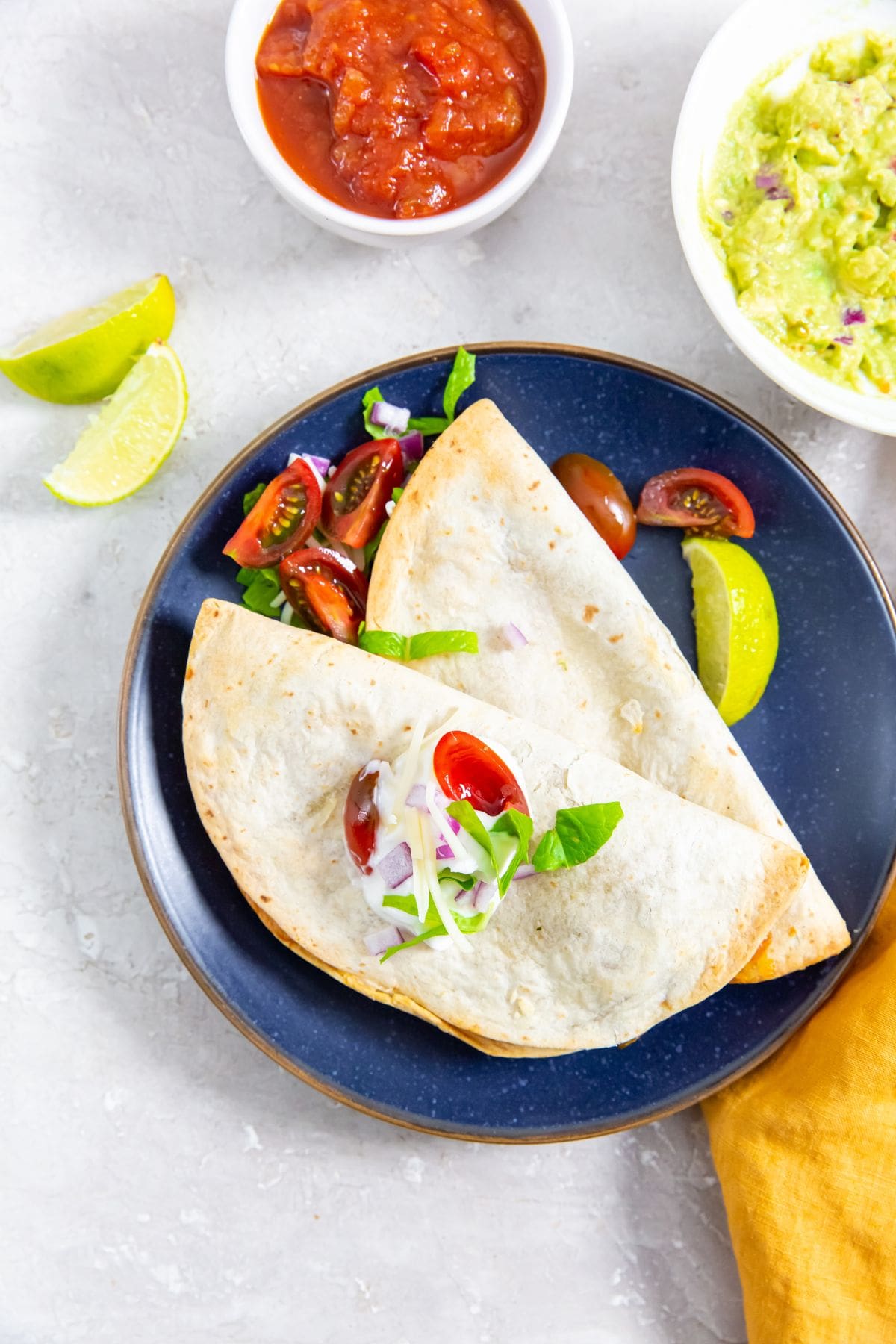 blue plate with an Air Fryer Trader Joe's Chicken Quesadilla on it. guacamole and salsa in the back.