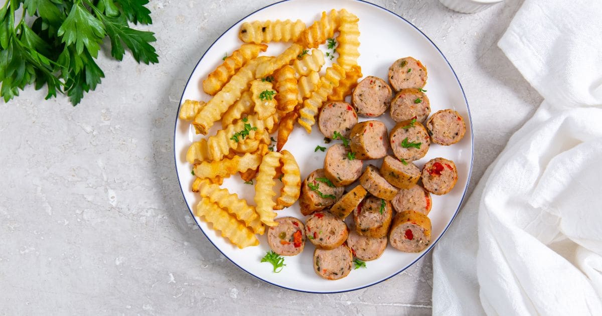 white plate with chicken sausage and fries on the plate. parsley, ketchup and white towel in the background