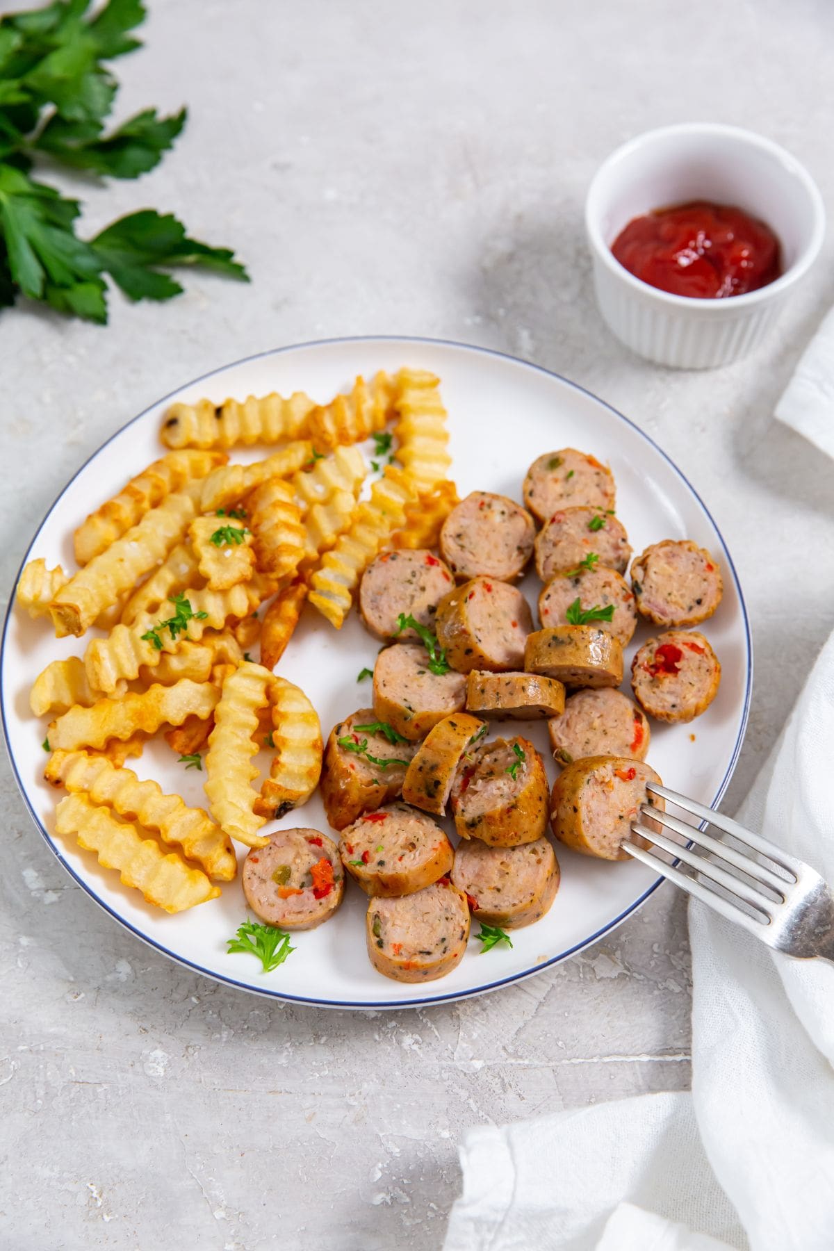 white plate with trader joe's spicy jalapeno chicken sausage and fries on the plate. parsley, ketchup and white towel in the background