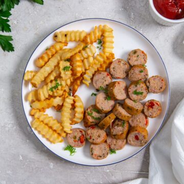 white plate with chicken sausage and fries on the plate. parsley, ketchup and white towel in the background