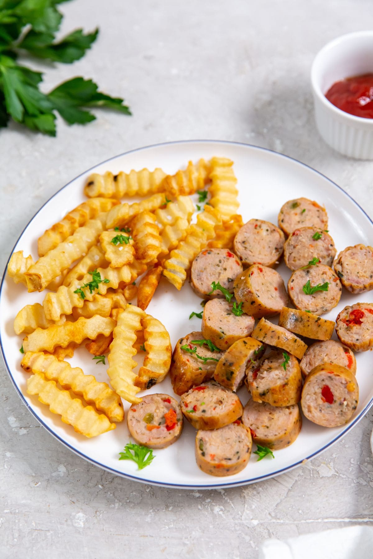 white plate with chicken sausage and fries on the plate. parsley, ketchup and white towel in the background