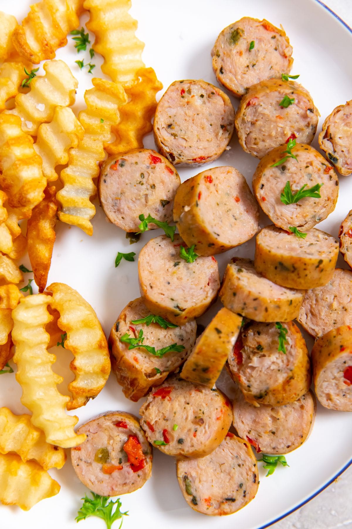 white plate with Air Fryer Trader Joe's Spicy Jalapeno Chicken Sausages and fries. parsley, ketchup and white towel in the background