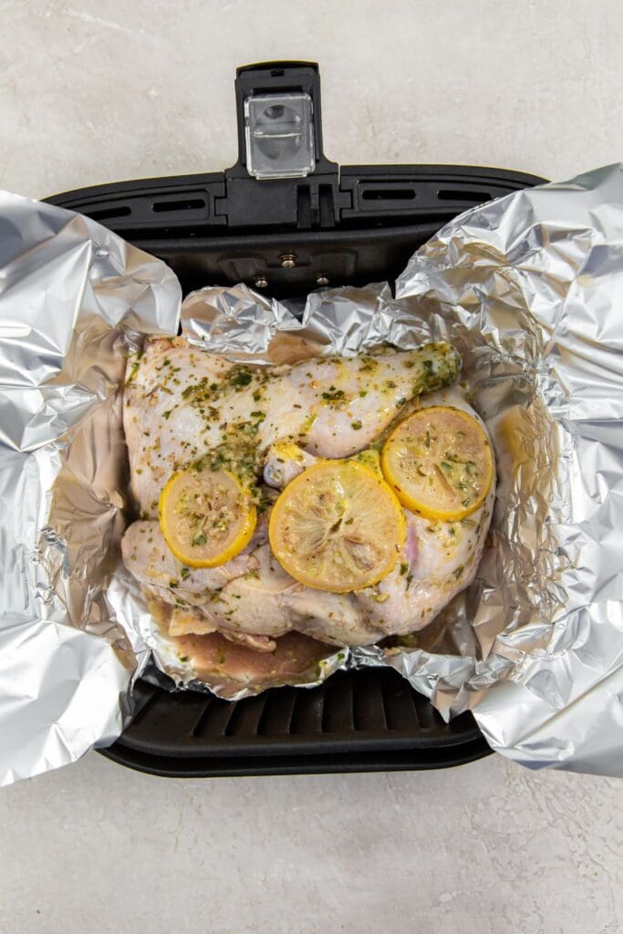 black air fryer basket with aluminum foil and chicken inside