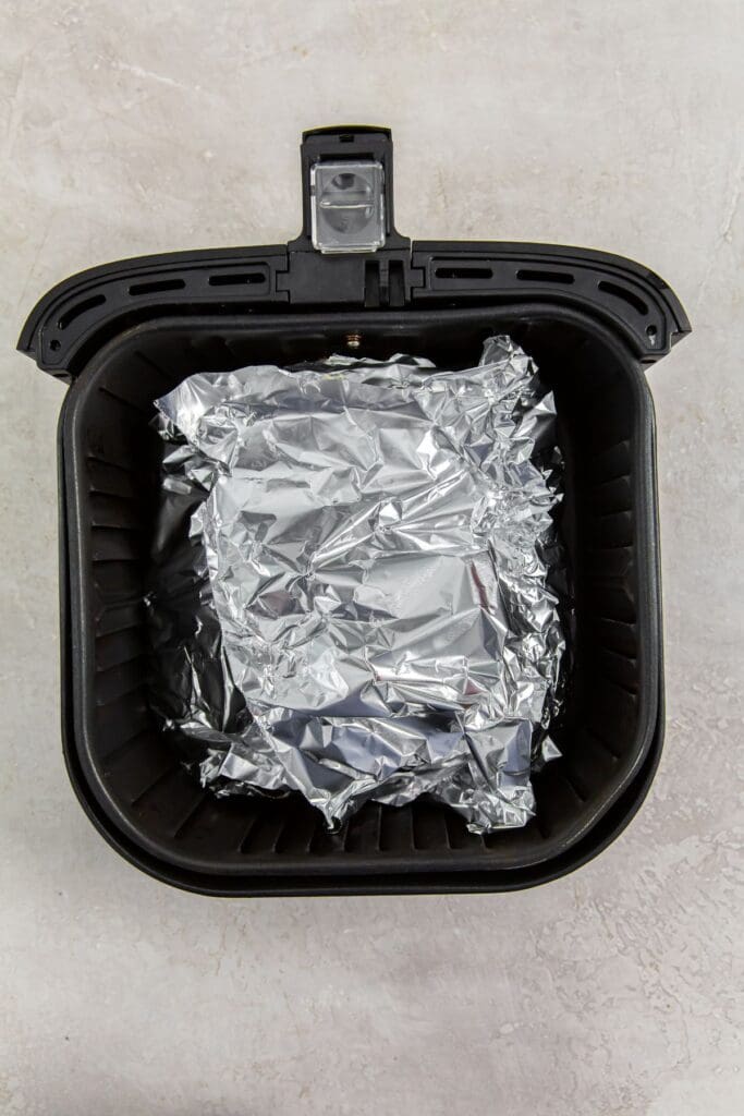 black air fryer basket with aluminum foil inside it