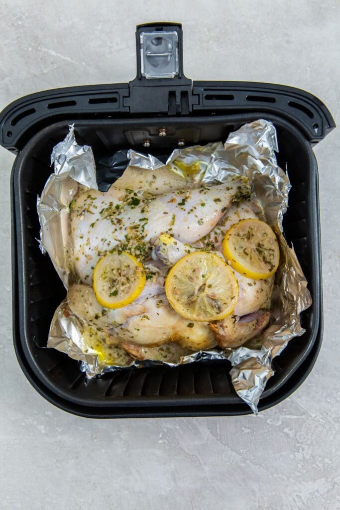 black air fryer basket with aluminum foil inside it and chicken