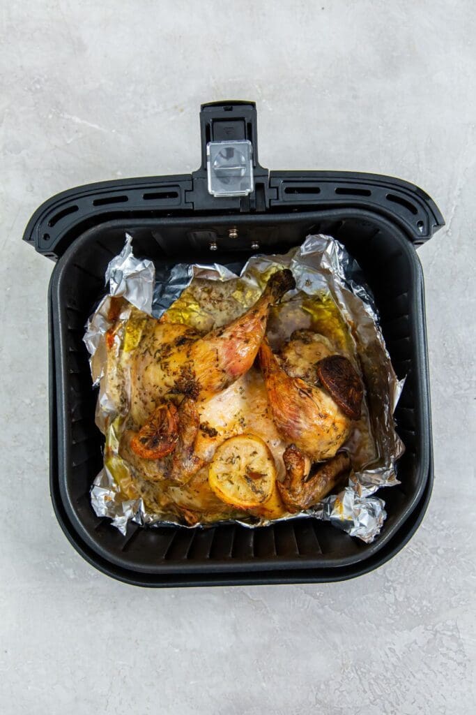 black air fryer basket with aluminum foil inside it and chicken