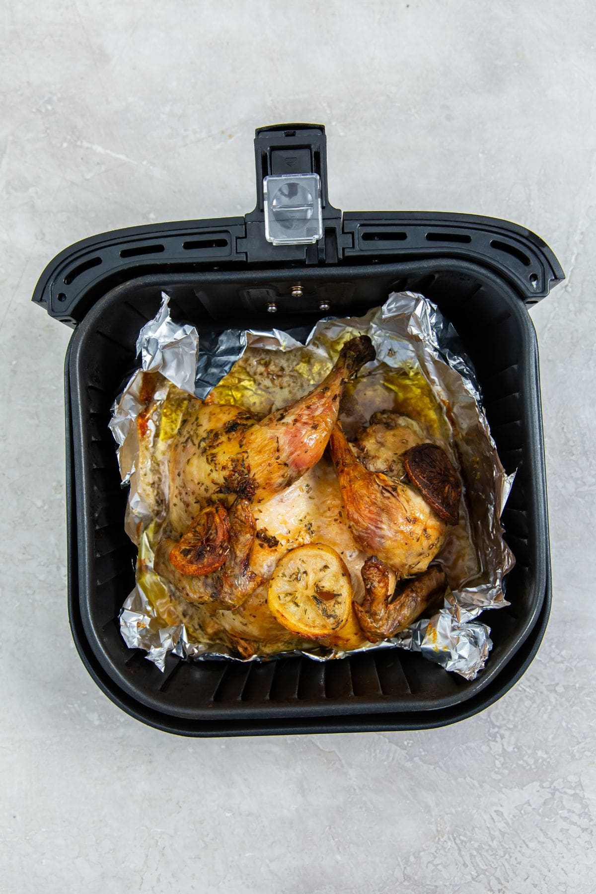 black air fryer basket with aluminum foil inside it and chicken