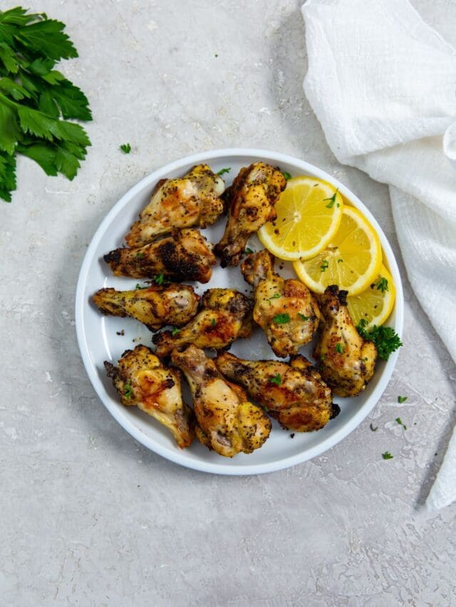 white plate with chicken and lemons on it. parsley in the back.