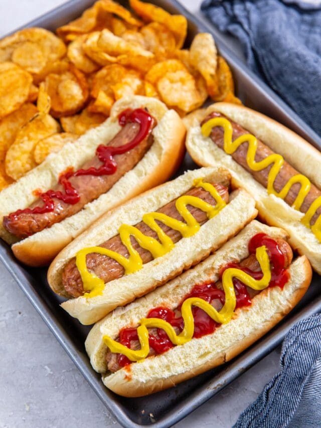 tray with chicken in a hotdog bun mustard and ketchup on top. chips on the side. blue towel behind it.