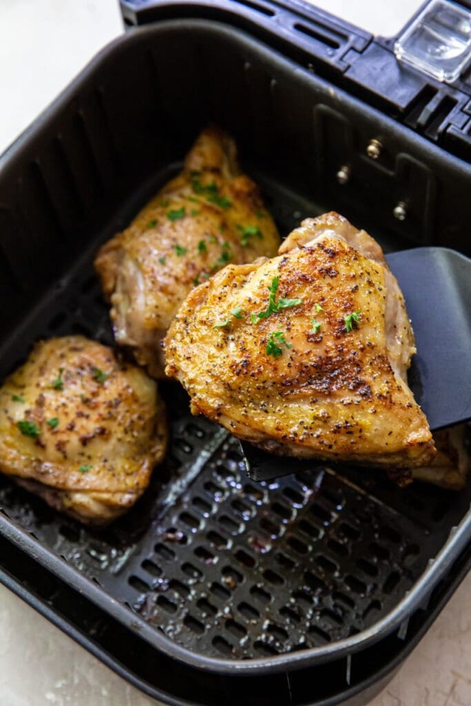 black air fryer basket with cooked chicken inside. spatula holding chicken