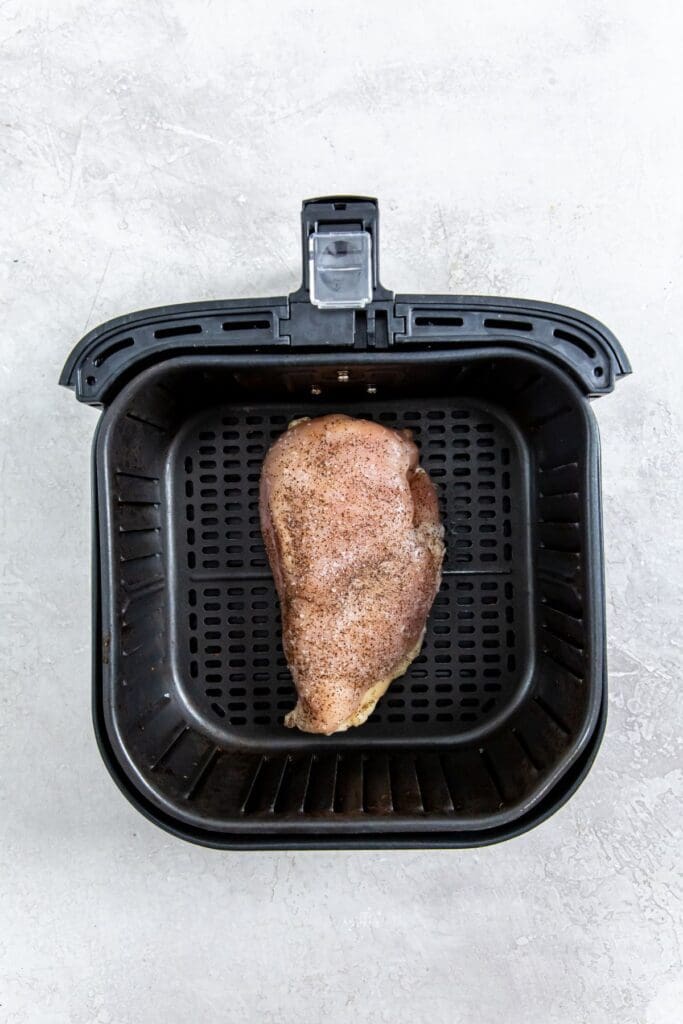 black air fryer with raw chicken inside