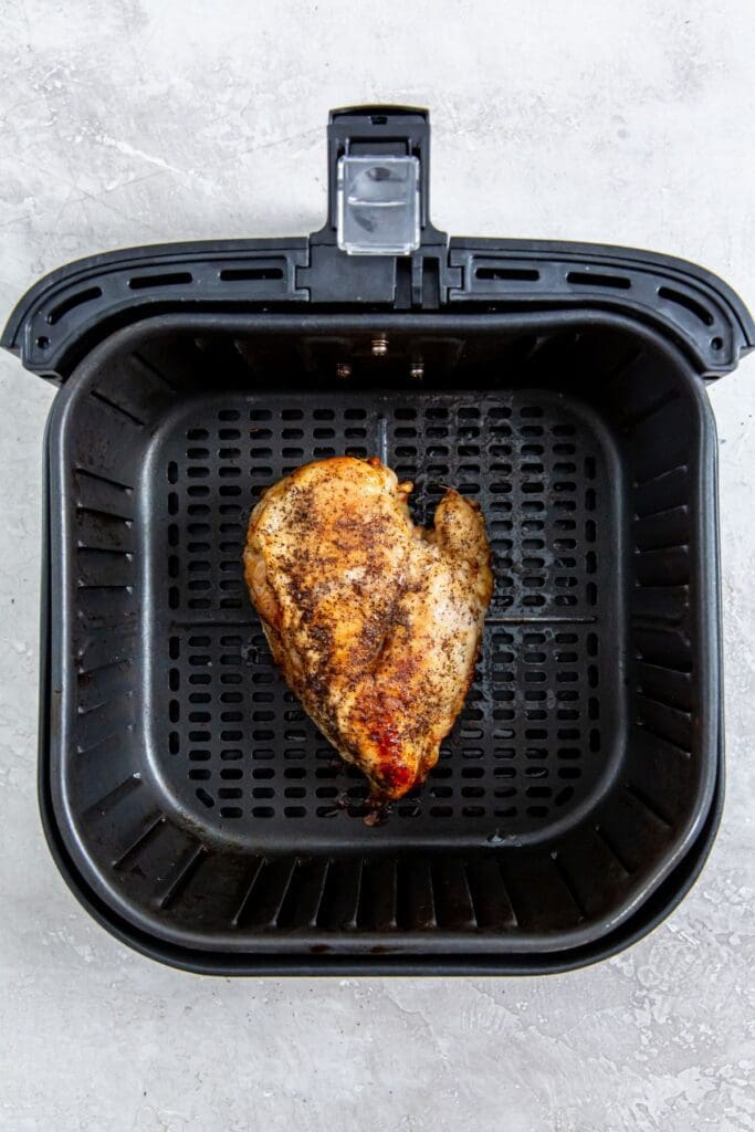 black air fryer with cooked chicken inside